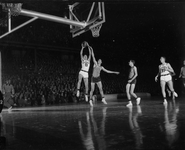 Tom Ketchum (#26), Loyola center at left, attempts to block Wisconsin's Albert "Ab" Nichols (#8), at right, from dunking the ball. The University of Wisconsin's basketball team defeated Loyola University's team 66-47.