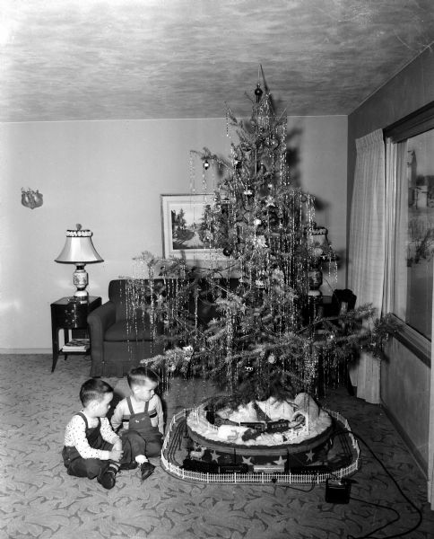Five-year-old Jimmy Lucas, at left, and his brother, three-year-old Jerry, the sons of Lee and Marcella Lucas, sit next to their Christmas tree at 466 South Owen Drive. The tree is set on an electric turntable, designed by their father, an engineer, and features an electric train in a winter setting.
