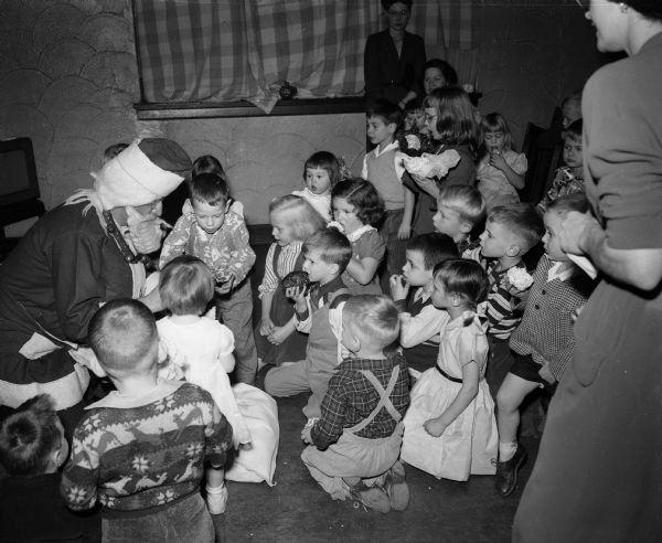 A group of children gather with Santa Claus at the annual children's Christmas party for children and grandchildren of University Club members. Adults assisting are Mrs. G.A. Rolilch, Marion Winans, and Helene Young.