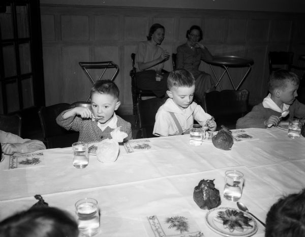 Three children eat ice cream at the annual Christmas party for children and grandchildren of University Club members. At left is Karl Rohlich and center, Tommy Rohlich.