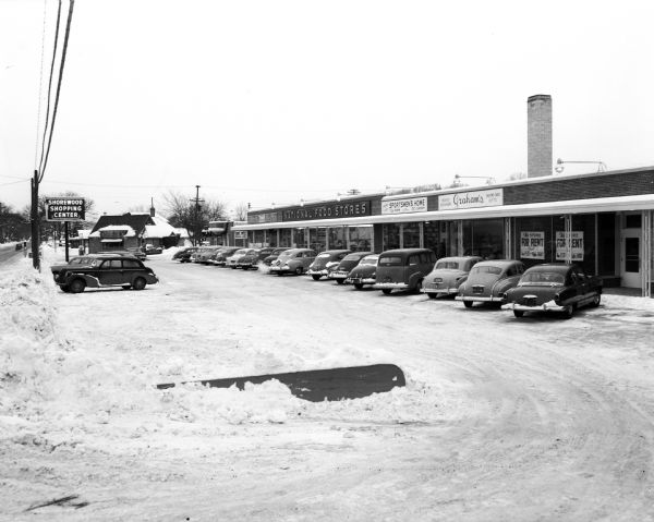 View of the Shorewood Shopping Center parking lot at 3244 University Avenue, looking west. Included in the photograph are the storefronts of the National Food Store, Graham's Book and Stationery Store and the Sportsmen's Home in Shrewood Hills. Frenchy's Restaurant, 3302 University Avenue, is in the background. An advertisement for the National Food Store appeared in the <i>Wisconsin State Journal</i> on January 1, 1952.