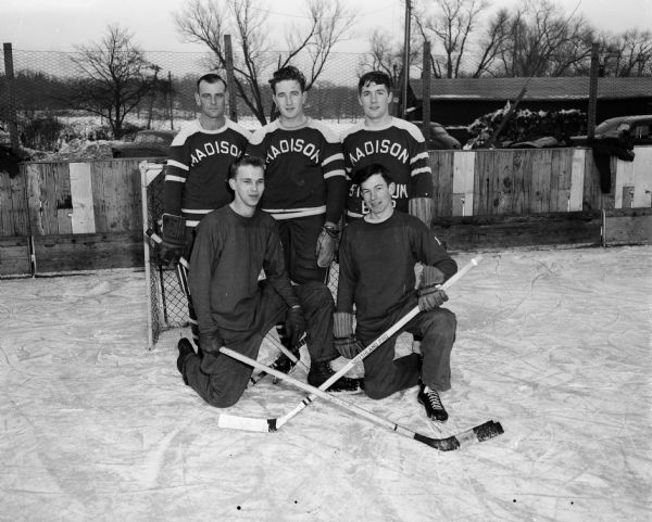 Group portrait of five members of the Madison Cardinals hockey club, gathered at Vilas Park for their first workout of the season. Pictured, standing left to right, are: Leo "Baldy" Fiscus, Johnny Riley, and John McCormick. Kneeling in front are: Jerry Vilbrandt (left) and Jerry Heinrichs.