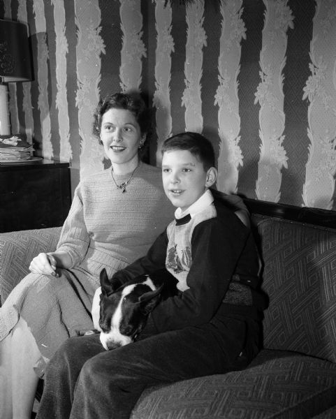 Bruce Chapman, age 12, is shown five years after being stricken with polio and recovering completely. His mother, Ferne Chapman, is sitting at left with their dog, Buster, in between them. Bruce's father (not pictured), Gordon Chapman, served as chairman of the National Foundation for Infantile Paralysis.