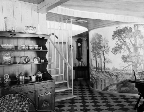 Interior view of the Doctor John Booher home overlooking the Baraboo river near Reedsburg. The photograph shows the hanging staircase — the bottom step does not touch the floor — and a mural done by a Reedsburg artist.