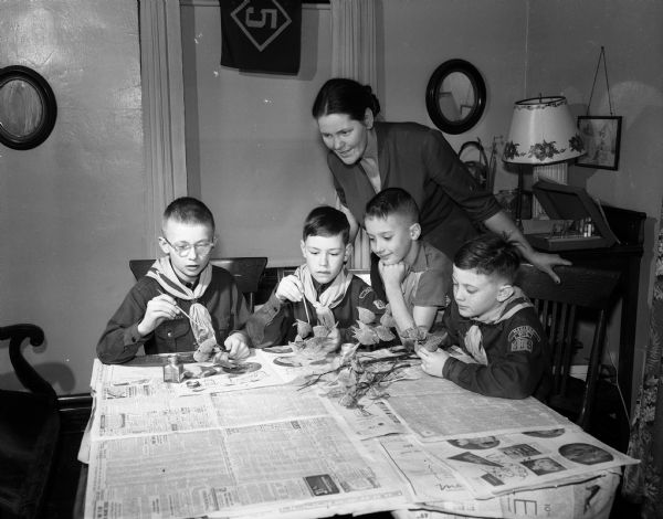 Four Cub Scouts painting milk pods as table decorations as den mother Mrytle Arnold is looking on. Scouts are, left to right: Dick Quale, David Arnold, Michael Lampman, and Michael Arnold.
