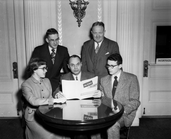 Portrait of the Council of Churches officials, three men and two teenagers, sitting around a table looking at a brochure titled: "The Call to United Christian Youth Action."