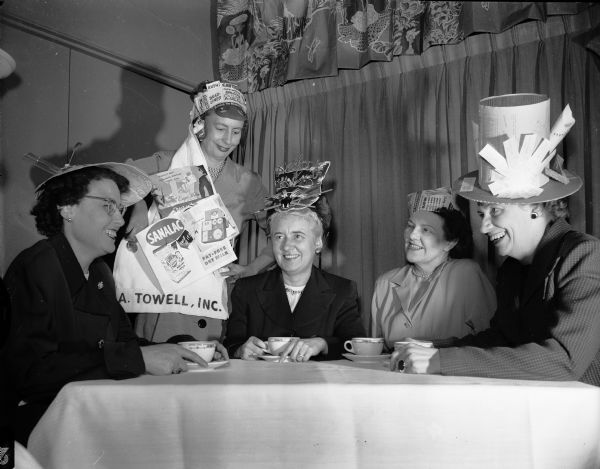 For the first time in the history of the Madison Advertising Club, the women members plan the dinner and program to be held at the Hoffman House. Hats made from materials used in their various types of advertising will be worn by the female members attending the dinner and program. Wearing some of the hats are, from left to right: Grace Kennedy, 4913 Midmoor Road; Marion Mills, Lake Mills; Lydia Jensen, 11 Cambridge Road; Viola Fitton, 121 S. Hamilton Street; amd Lela Josephson, 226 Van Deusen Street.