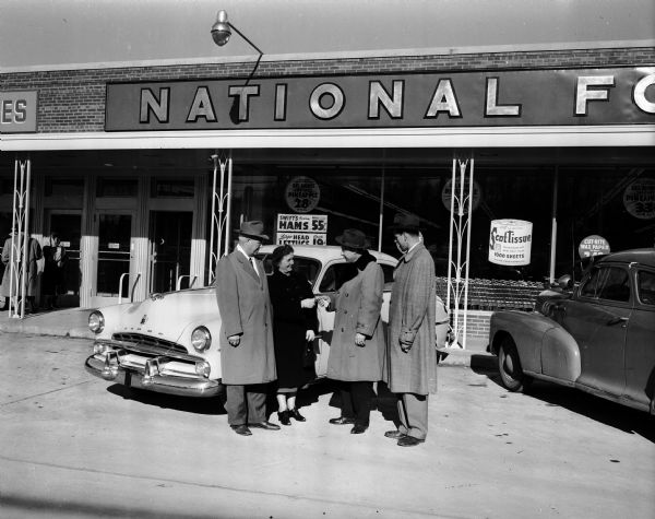Mrs. J.E. Stallard, writer of the winning sentence starting "I like to shop at National Food Stores because..." is shown with her husband, Professor Stallard, as she receives the keys to her new 1952 Dodge from Dan Dary, District Sales Manager, and Bill Tuchlinsky, Manager of the University Avenue Store of National Food Stores, at 3244 University Avenue.