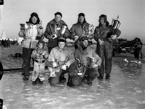 Winners in the Northwestern Ice Yachting Association ice regatta hold their trophies after the races held on Lake Monona. Left to right, front row, are: William (Spike) Boston, "youngest skipper in the meet"; Dan Coffey, Menominee, Michigan, Class B winner; and Don Ward, Menominee, Michigan, Class D winner. Back row, left to right, are: Carl Bernard, Madison, Class A winner; Bud Stroshine, Oshkosh, Class C winner; Elmer Millenbach, Detroit, Michigan, free-for-all winner; and Bill Perrigo, Pewaukee, Class E winner.