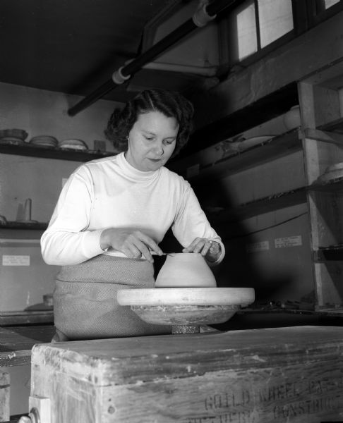 The junior division of the University of Wisconsin Service League for faculty wives has a number of interest groups including the handicrafts group. Mrs. Warren Gabelman, 31-B, University Houses, is pictured concentrating on trimming the feet of a bowl that she is making in the Daniels Art Studio at 419 West Gilman Street where group members do their work.