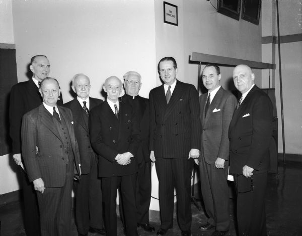 Group portrait of officials who took part in the dedication program for the new University of Wisconsin cancer research hospital. Left to right are Former State Representative Frank Keefe, Medical School Dean William Middleton, Board of Regents President Frank Sensenbrenner, Regent William Campbell, Madison Catholic Bishop William O'Connor, United States Surgeon General Leonard Scheele, Governor Walter Kohler, and University of Wisconsin President Edwin B. Fred.
