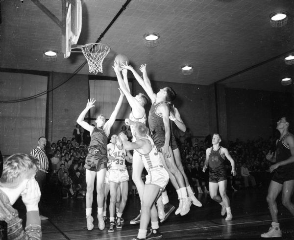 West High School's John Parker (36 in white uniform) takes a rebound off the Kenosha High School basket during an intense game which West finally won 50-54. Other West players are Tom Mack (33), and Jim Mahoney (37.) Kenosha players in the dark uniforms are Captain Leo Time (17), Tom Udahen (12), Bob Girman (14), and Bob Buters (5).