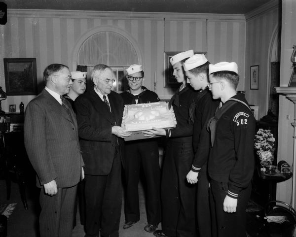 Five Sea Scouts surprise former State Supreme Court Chief Justice Marvin B. Rosenberry with a birthday cake on his eighty-fourth birthday. He has been presented with a cake each year by the Scouts. The former Chief Justice could not attend the Boy Scout ceremonies in the State Historical Society because of illness, so the Scouts brought the cake to his home. Pictured from left to right are Grover Broadfoot, Supreme Court Justice; Nello Lansdowne, Marvin B. Rosenberry, former Chief Justice; Glynn Narum, Arlyn Jones, Charles Kennedy, and John Price.