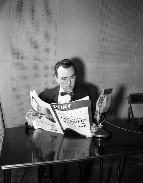 John B. Davies, news editor for radio station WKOW, reads into a microphone from the Saturday Evening Post magazine in his hands.
