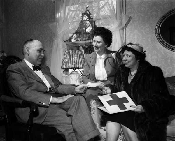 The work of the Red Cross in peacetime is less well publicized than its wartime services. Mrs. Thomas J. (Mildred) Pattison, 2024 Kendall Avenue, residential chairman for the 1952 Red Cross fund drive, at right, is pictured receiving a check for the drive from Lucien Schlimgen, 2022 Kendall Avenue, left, and his wife, Angela, center.