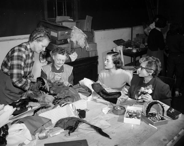 The members of the Madison Theater Guild have worked seven days a week to make costumes for a cast of 30 in the production of "As You Like It". They are working in the new sewing room at the workshop, a warehouse on East Main. Shown left to right are the designer who uses only the name Loie; Julia Mailer, chairman of the costume committee; Marie Helgerson; Ruth Foster; and Eleanor Grant. Committee members not pictured are Doris Farmiloe, Mae Merriman, and Marilou Durkin.