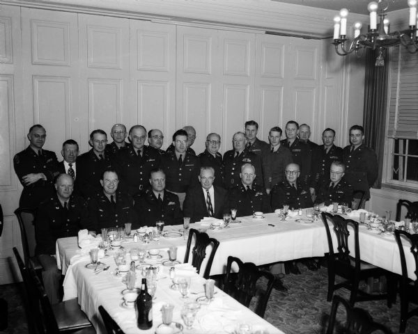 23 uniformed attendees at a National Guard banquet stand behind a banquet table for a portrait.