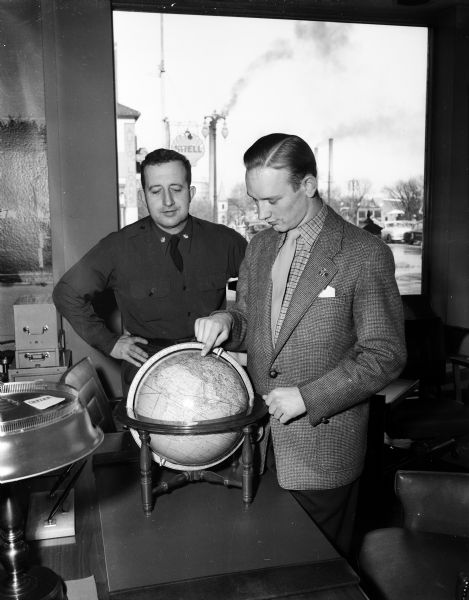 Twenty-two year-old Danish immigrant, Neils Lassen, right, uses a globe map to point out his native Denmark to Major Roberts of the Madison Army and Air Force recruiting station.  Lassen, who came to Madison seeking an education at the University of Wisconsin and has been in this country only seven months, enlisted in the Air Force at the Madison recruiting station.