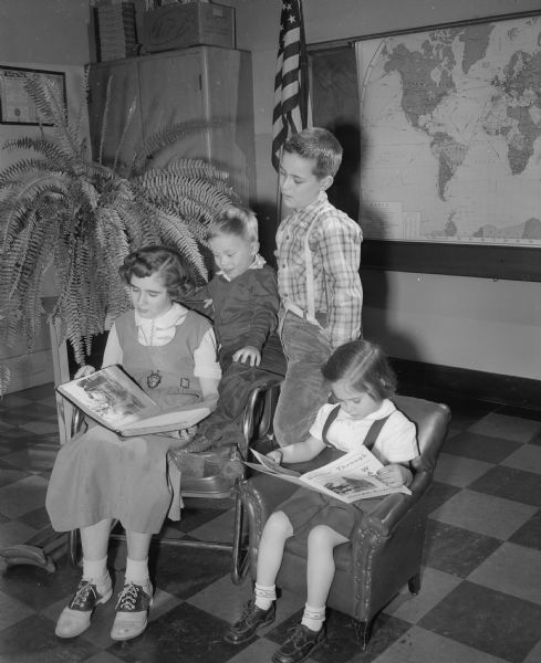Looking at scrapbooks of Camp Wawbeek are four pupils who attend the special orthopedic department at the Washington school in Madison. Camp Wawbeek, located at Wisconsin Dells, is the recreational camp for children and adults with handicaps. The camp is one of the several projects maintained by the sale of Easter Seals in Wisconsin. From left to right, the children are Ann Higgins, Paul Rosen, Douglas Wenger, and Susan Dye.