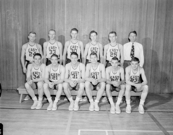 Group portrait of the Madison East high school basketball team. In the first row are, left to right: Herb Hanson, Jim Kurth, Charlie Brendler, Gary Wold, Rollie Wessinger, and Gordy Morris. In the back row, left to right, are: Dick Krier, Paul Thomsen, Charles Jones, Ted Blackney, Dick Simonson, and coach Milt Diehl.
