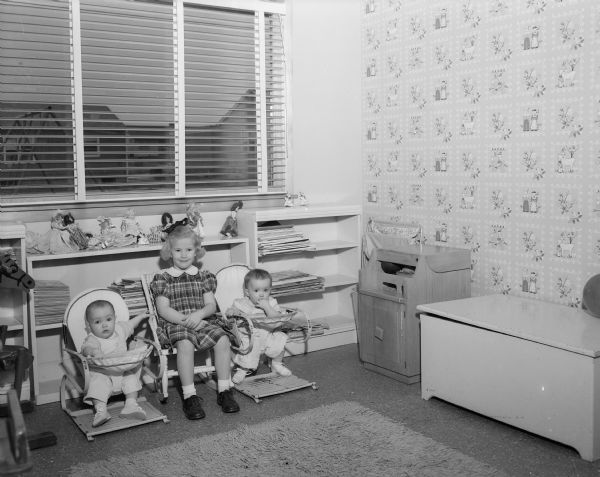 Interior view of the playroom in the home of builder Tom McGovern and his wife Ruth at 25 Hiawatha Circle. The couple's five daughters, three of whom are pictured here, spend most of their time in this spacious room, part of a children's wing of the house that also contains four bedrooms and two bathrooms. Pictured left to right are: Des, Terry, and Lee. Des and Lee are ten-month-old twins and Terry is four-and-a-half.