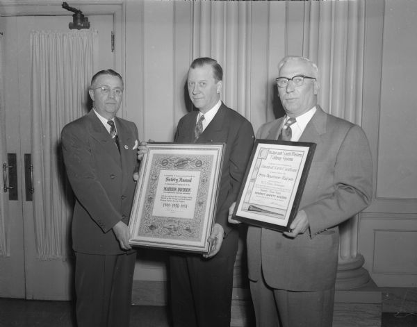 Three men are shown with two awards commemorating North Western railroad safety. P.E. Feucht, executive vice-president (center), presented the Madison division with a plaque for having the best safety record of the entire system for the third straight year. L.G. Reynolds (left), Madison division superintendent, accepted the award in behalf of the division's 2,000 employees. Also receiving an award was W.A. Vallely (right), storekeeper at Madison whose department has had no lost-time accidents for 23 years.