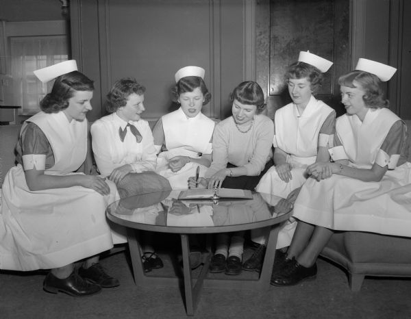 Shown are six members of the Wisconsin State Student Nurses' association at the University of Wisconsin. From left to right, they are Marilyn Hall, Lexy Nesson, Dorthy Dawson, Ellen Duwe, Norma Waelti, and Katinka Conger. They are preparing for the spring convention. Twenty-four state schools of nursing are members of the association. Four of the six women are wearing nurse smocks, nurse caps and sensible shoes.