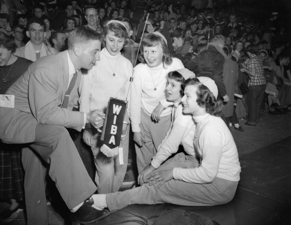 Wisconsin State High School basketball tournament at the University of Wisconsin-Madison Field House. Roger Forster, announcer from radio station WIBA, interviews Tomah's cheerleaders. Forster introduced something new at the state basketball tournament by use of a midget radio transmitter for his interviews.