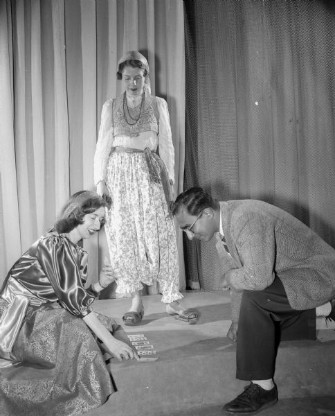 Participants at the University of Wisconsin International Club Costume Ball. Standing is Marian Kurick of Czecko-Slovakian descent, wearing a gypsy costume. Kneeling at left is Mary Walters wearing a Muslim costume, brought to this country from Albania by her mother. Kneeling at right is Manick Gupta of Bombay India. 
