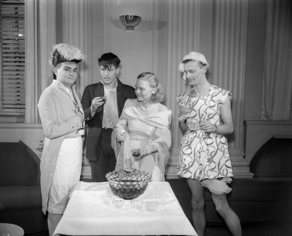 Four participants at the University of Wisconsin International Club Costume Ball gathered at the punch bowl. Left to right: Martin Begus, dressed as Napoleon; Russell Webber, club president; Delores Nemee; and Alan MacDiarmid, wearing a women's dress, "A foreigner's interpretation of an American glamor girl".