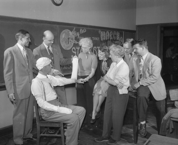Madison teachers participating in a Red Cross first aid training course as part of the civil defense program. West high school principal R. O. Christoffersen serves as the "victim" for a class in bandaging. Other teachers looking on are, left to right, Charles Steinmetz, Dalton Hedlund, Beatrice Walton, Mrs. Vivian Seiverd, Marion Huxtable, Parnell Bach, and C.J. Antonie.