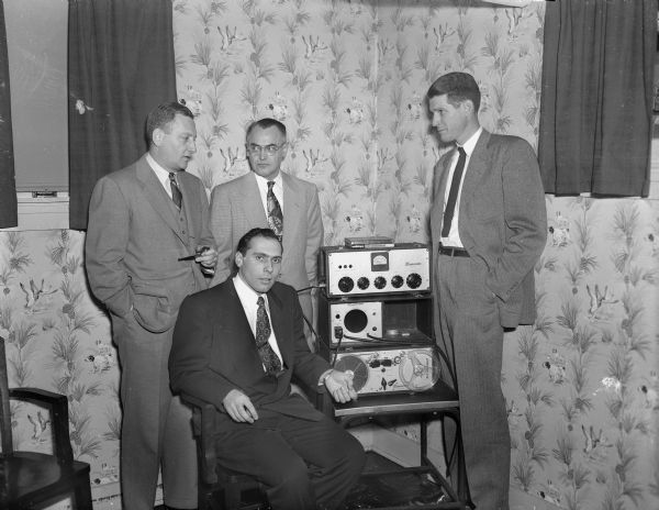 Four members of a Dane County Medical Society Committee are sitting and standing around tape recording machinery. They had edited a sound tape recording of the birth of a baby to be used in the program "Birth of a Baby." The program would be broadcast on a local radio program on station WISC and later on a national network. It was the first such event in radio history.
