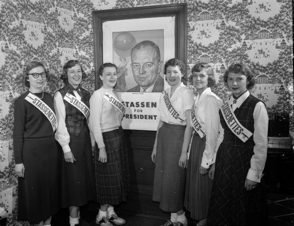 Six University of Wisconsin co-eds wearing "Stassenettes" sashes posing in front of a "Stassen for President" poster when the presidential candidate spoke at a rally on the University of Wisconsin campus.