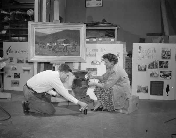 Donald Haugen and Mrs. William F. Ackerman painting a coal stove which is part of a school room setting to be used for the display of the Winslow Homer painting "Snap the Whip". The painting is one of 14 famous paintings on display in the Madison Art Association exhibit titled "American Open House — 200 Years of Art in Its Time." The displays are set up as 10 periods tracing art and life in America. Each of 14 famous paintings is installed as the central piece in an arrangement of furniture, fabrics, utensils, and costumes designed to place it within its period in American life.