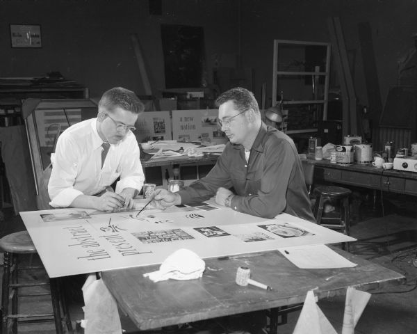 Richard Houghton, left, and Charles Haycock, assistant curators of exhibits at the Wisconsin Historical Museum, working on a descriptive background panel for the "Abstract Present" display of the Madison Art Association exhibit titled "American Open House — 200 Years of Art in Its Time." The displays are set up as 10 periods tracing art and life in America. Each of 14 famous paintings is installed as the central piece in an arrangement of furniture, fabrics, utensils, and costumes designed to place it within its period in American life. The Wisconsin Historical Museum prepared the descriptive background panels and furnished many of the pieces for the displays.