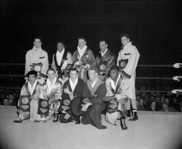 Group portrait of 10 individual champions of the NCAA boxing tournament held at the UW fieldhouse.  Front row, l to r: Roy Kukboyama, Hawaii, 112; Frankie Echevarris, Idaho, 119; Neil Ofsthun, Minnesota, 125; Archie Slaten, Miami, 132, and Chuck Adkins, San Jose State, 139. Back row, l to r: Bobby Morgan, Wisconsin 147; Ellsworth Webb, Idaho State, 156; Gordon Gladson, Washington State, 165; Charlie Spieser, Michigan State, 176; and Bobby Ranck, Wisconsin, heavyweight.