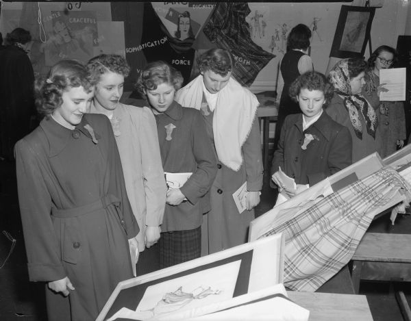 Five girls from Rio High School are studying an exhibit of dressmaking and dress design.  Left to right are Frances Traut, Donna Mae Hebel, Jeanette Wruck, Josephine Patroeli and Elvira Krinke.