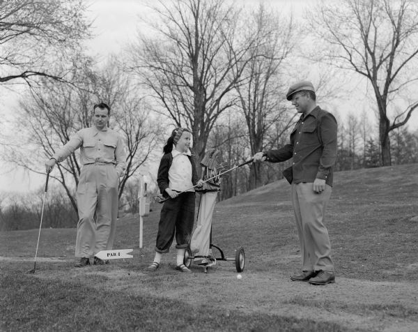 Richard Ratcliff, a University of Wisconsin professor, is receiving his driver from his daughter, Becky, who acted as his caddy.  John H. Westing is at the left. They were golfing at Blackhawk Country Club golf course.