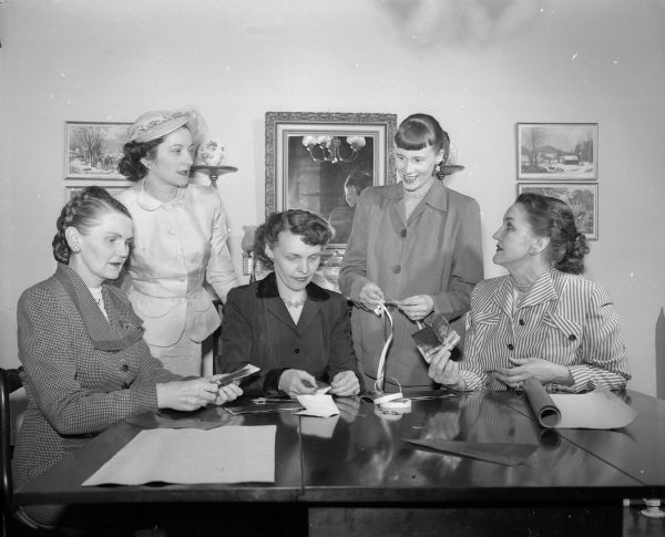 Five naval officers' wives making plans for the May dinner dance of the Naval Officers' and Wives' Club. Seated, left to right, are: Mrs. A.F. (Emily A.) Ahearn; Mrs. R.L. (Maxine C.) Kulzick; and Mrs. W.G. (Ethel H.) Martin.  Standing, left to right, are: Mrs. S.D. (Harriet J.) Kelly; and Mrs. R.J. (Janet R.) Huegel.