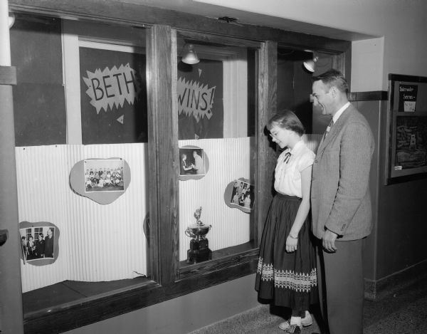 Beth Knope, 13-year-old champion of the <i>Wisconsin State Journal's</i> 1952 Badger Spelling Bee, with Walter W. Engelke, the principal of Nakoma school, admiring the school trophy case with a display devoted to her.