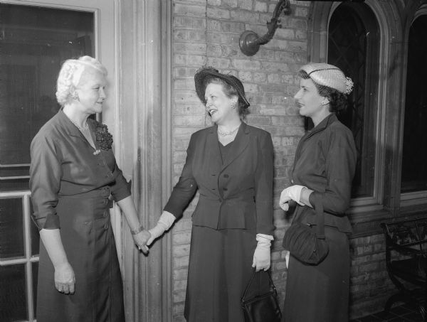 Mrs. Oscar (Mary F.) Rennebohm, a member of the UW-Madison chapter of the Gamma Phi Beta Mothers' club, at the door of the sorority house as she welcomes two guests for a benefit bridge party. Mrs. Wayne (Helen R.) Loveland, middle, and Mrs. Vance (Marie E.) Dean, right, are the two guests.