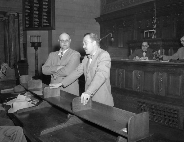 Adolph Maasen (left), the leader of a group of state farmers claiming prejudice against farmers by the State Selective Service, observing Colonel Bentley Courtenay addressing the group in the state assembly chamber. Mr. Courtenay is the state draft head.