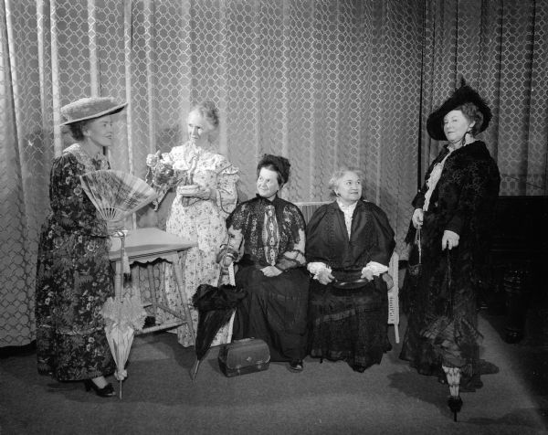 Five women in costume, acting in a scene from "Gay Nineties," a skit written by Lorraine Rucker for the Drama and History departments of the Madison Woman's Club. In the scene, the women are telling about their visits to the 1893 Columbian Exposition in Chicago. Actress's, left to right: Lorraine Rucker, Leslie Van Hagan, Elle Carter, Fannie Mack, and Sarah Rasmussen.