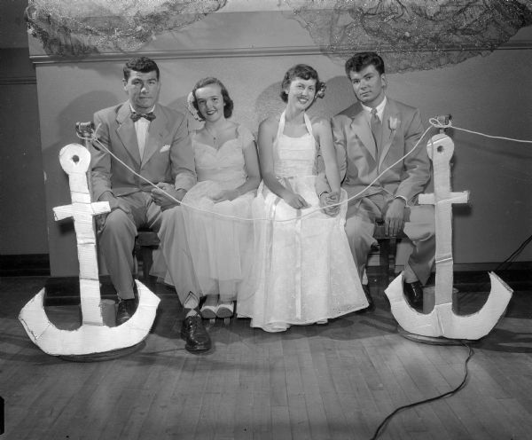 Two couples in formal dress are seated between two large prop anchors. They are Norbert Esser and Susan Hunt (left), and Marcia Pilon with Jim Corcoran (right).