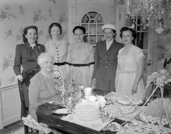 Six members of the Who's New club at a tea at the home of Mrs. Oscar Rennebohm. Seated is Mrs. Milo Kittleson. Standing from left to right are:  Mrs. L.M. Doty, Mrs. R.K. Phillips, Mrs. C.S. Van Sickle, Mrs. D.R. Syvrud, and Mrs. D.E. Teifert.