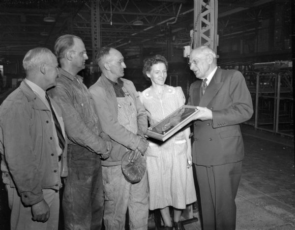 Four men and one woman with the Research Products Award (a plaque) inside an industrial looking building.