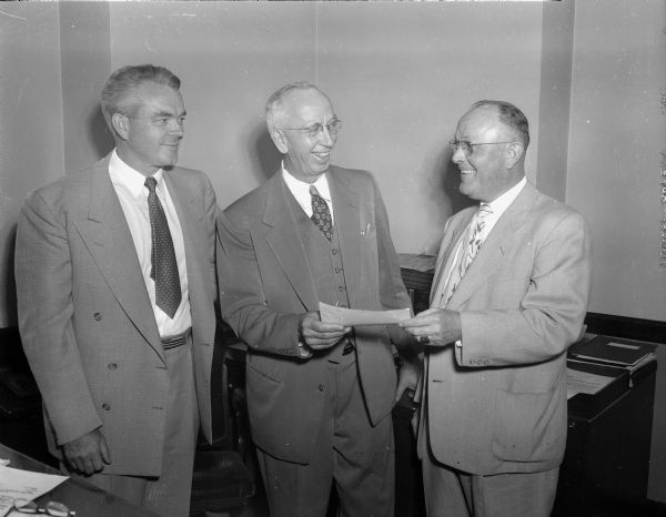 Three men, one of whom is handing a check to one of the other two men, for the Wisconsin Telephone Company.