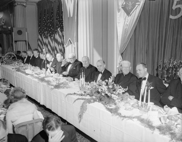 The head table of the Golden Jubilee convention banquet of the Wisconsin Knights of Columbus held at the Loraine Hotel in Madison. From right to left are: Governor Walter Kohler; Bishop William P. O'Conner, Madison; Judge Harold J. Lamboley, Monroe, district deputy; John P. Treacy, LaCrosse, director; Charles W. Henney, Portage, supreme director; the Right Reverend E.J. Westenberger, Green Bay, state chaplain; Leslie J. Schlax, Kenosha, state secretary; Donald W. Gleason, Green Bay, state advocate; the Reverend Jerome Mersberger, chaplain of the Madison council; L. Matthew Larson, grand knight of the Madison council; and Frank Byrne, past grand knight of the Madison council.