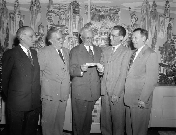 Oscar Rennebohm, president of Rennebohm Drug Stores, Inc., welcoming two new members to the Rennebohm Drug Store 25-year club at the firm's annual pension trust banquet in the Madison club. Rennebohm is presenting checks of $1,250 to the men, Oscar Henning, second from right, pharmacist in charge of pharmaceuticals at the Rennebohm warehouse, and Wilbur Bakke, far right, vice-president in charge of store operations. Also pictured are George S. Schiefelbein, far left, manager of store No. 2 at 204 State Street (30 years), and Jack Healy, second from left, manager of store No. 3, at 13 W. Main Street (28 years). Rennebohm has been with the company for 40 years.