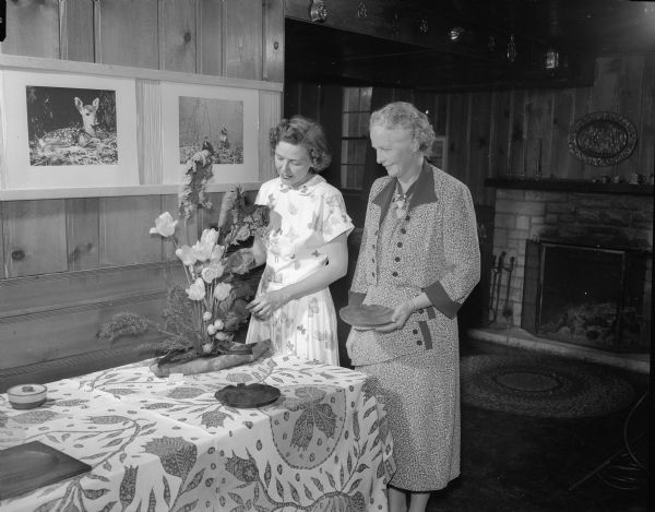 Garden show and tea at which the West Side Garden club entertained other garden clubs of the Madison area. June D. (Mrs. Robert) McLean, left, and Helen M. (Mrs. R.O.) Wissler, right, admiring a cut-flower arrangement on a buffet table at a home at 2310 Gilbert Road.